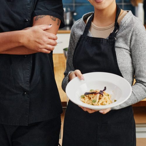 Diverse group of people wearing aprons and holding gourmet dishes in professional kitchen